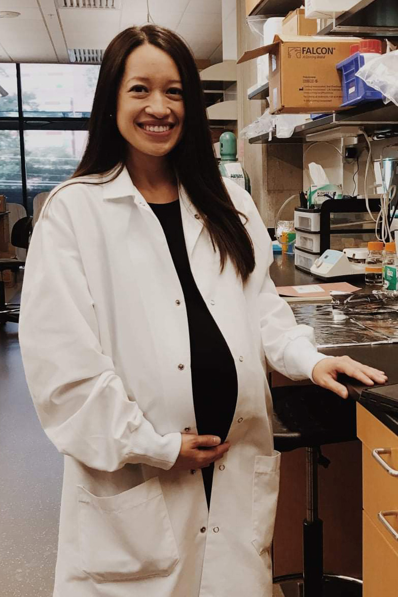 A pregnant Midori Wasielewski in lab coat stands in her lab at Georgia Tech.