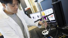 Mechanical engineering Ph.D. student Hohyun “Henry” Lee with the algorithm-controlled focused ultrasound system he developed. Lee is adjusting a metal arm that holds the ultrasound transducer and receiver with a computer behind him displaying information from the control algorithm.