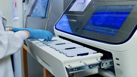 A hand with a blue glove placing a pipette tip tray into the Sanger Sequencing Machine