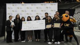 Photo of a group of nine students representing teams AdvanCED and Jawws holding a check for $1000. Two female students on the right side of the photo are holding small plaques. Next to the students on the far right of the photo is the Buzz mascot and Dr. James Stubbs, faculty advisor for BME Capstone.