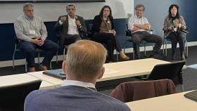 Photo of five McCamish conference panelists. Four panelists (one man and three women) listen to the fourth participant, a male, speaking.