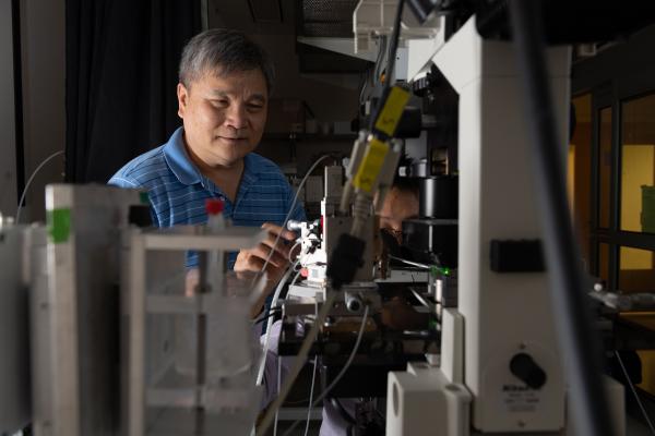 Cheng Zhu in his lab at Georgia Tech stands over a microscope station set up to observe forces researchers exert and measure on structures of living cells. Georgia Tech / Allison Carter