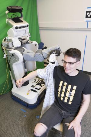 A PR2 robot puts a gown on Henry Clever, a member of the research team.