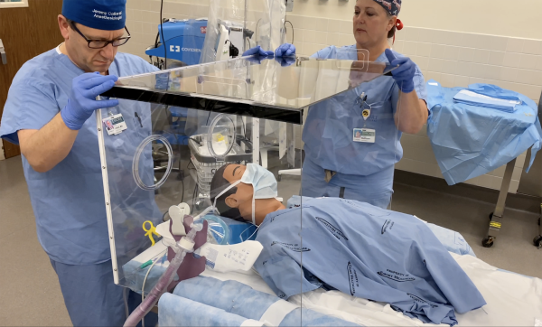 Jeremy Collins and Cinnamon Sullivan demonstrate a barrier protection device designed for use curing the COVID-19 pandemic. Collins is associate professor of anesthesiology and executive vice chair of anesthesia at Emory and Sullivan is assistant professor of anesthesiology, Emory University School of Medicine and the director of Global Health Anesthesiology at Emory University Hospital. (Credit: Emory Healthcare)