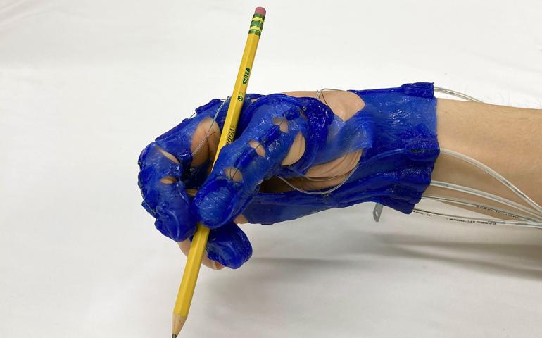 Blue hand exoskeleton glove gripping a pencil